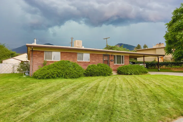 Brick exterior with a covered carport, mature shrubbery, and expansive front lawn