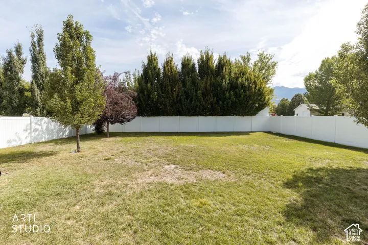 Expansive grassy yard with a full perimeter privacy fence, mature trees, and natural mountain backdrop