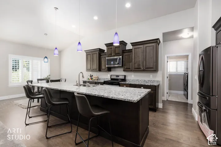 Kitchen featuring a large island with stone countertop, dark wood-finish cabinetry, stainless steel appliances, and wood-finish flooring