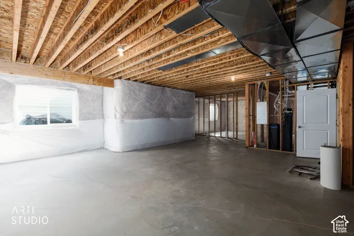 Unfinished basement featuring exposed wood joists, concrete flooring, framed interior walls, and a white window