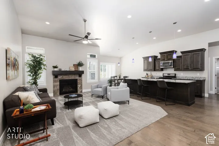 Vaulted ceilings with recessed lighting, stone-clad fireplace, built-in kitchen cabinetry, and wood-finish flooring