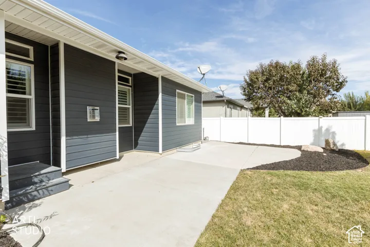 Exterior featuring dark siding, white trim, a concrete patio, a partial lawn, and a white privacy fence