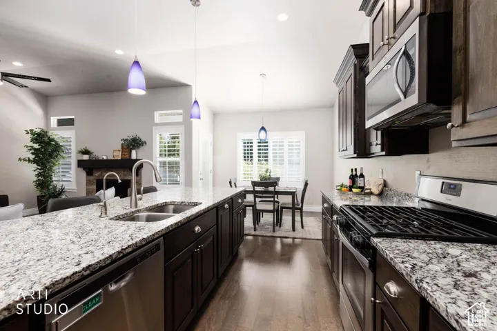 Kitchen featuring a large central island with double basin sink, stainless steel appliances, dark wood-finish cabinetry, and light-toned countertops