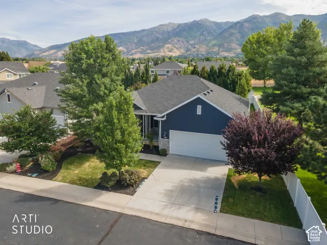 Dark blue siding exterior with stone accents, concrete driveway, attached two-car garage, and established landscaping