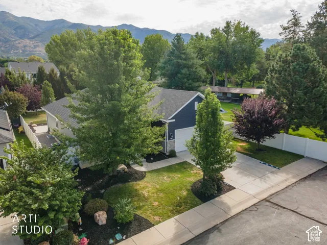 Mountain backdrop, expansive driveway, established landscaping, white privacy fence, and attached two-car garage