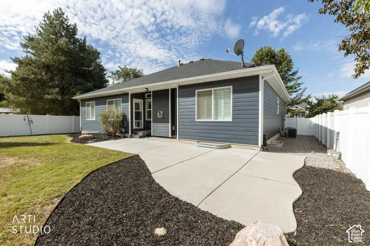 Expansive rear patio with concrete paving, siding exterior, mature trees, and white privacy fencing