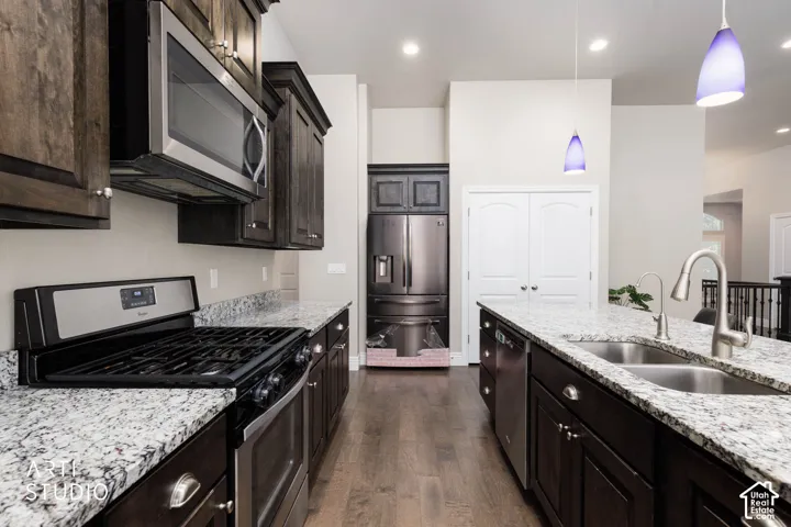 Kitchen featuring dark wood cabinetry, light speckled countertops, stainless steel appliances, and a dual basin sink with a gooseneck faucet