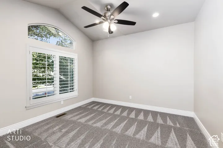 Vaulted ceiling featuring a ceiling fan with integrated lighting, arched window, plantation shutters, and patterned carpeting