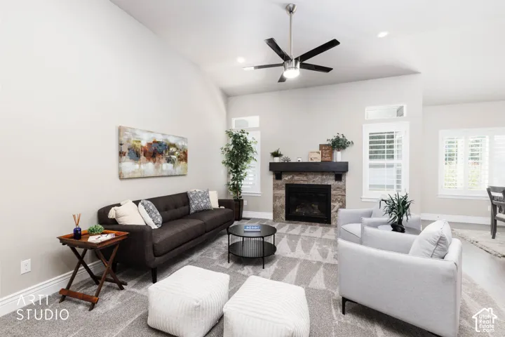 Vaulted ceiling with a contemporary ceiling fan, stone-clad fireplace with a dark wood mantel, plantation shutters, and recessed lighting