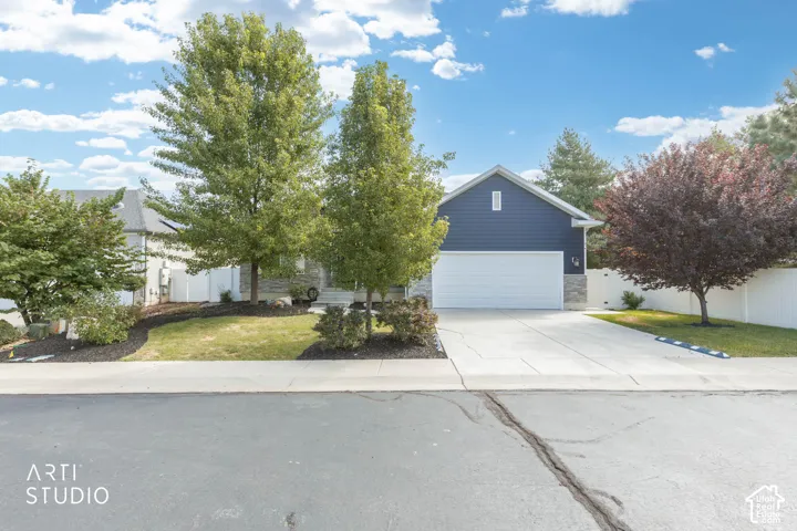 Siding exterior with stone accents, a concrete driveway, an attached garage, and mature landscaping