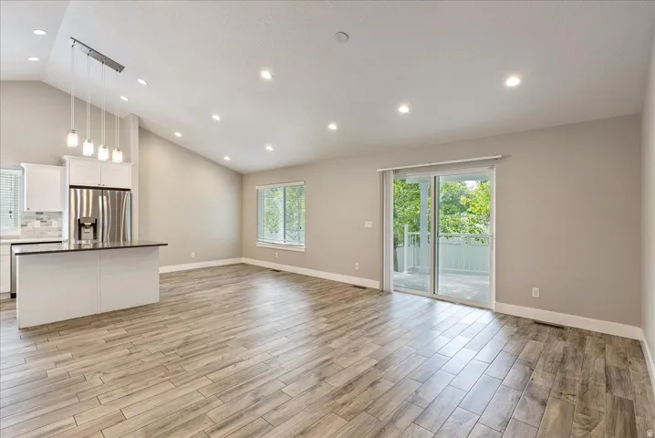 Vaulted ceilings with recessed lighting, wood-finish flooring, white cabinetry, stainless steel refrigerator, and glass sliding doors leading to an exterior balcony