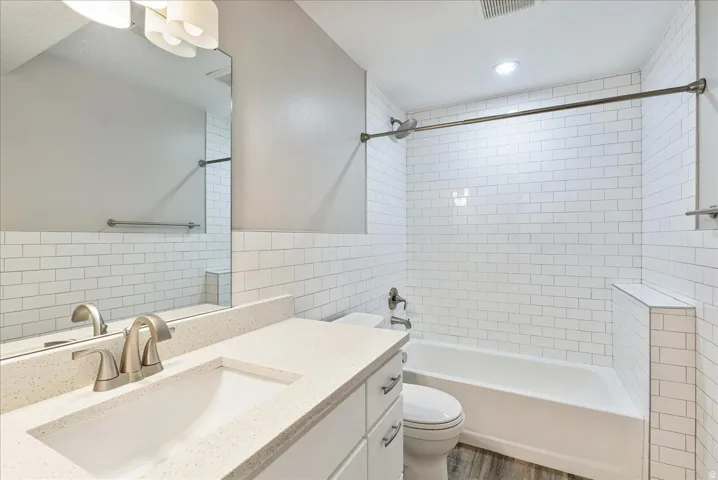 Bathroom featuring a white subway tile surround, a built-in bathtub, a vanity with a light-colored countertop, and a large wall-mounted mirror