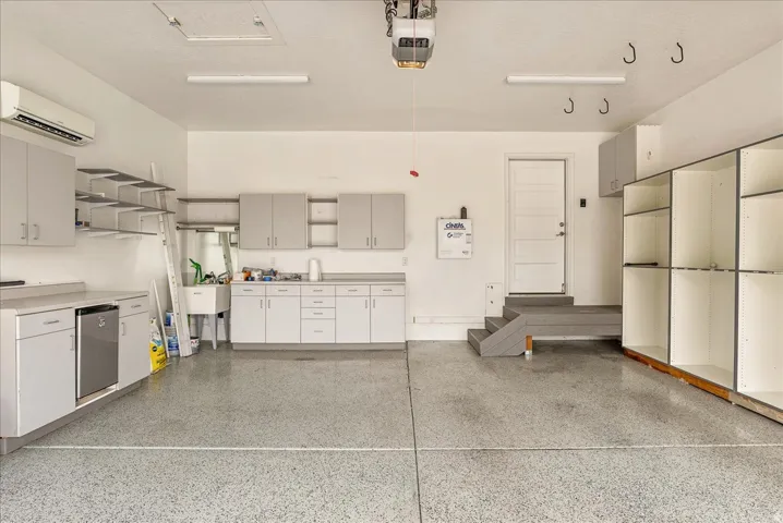 Garage featuring a finished epoxy floor, built-in cabinetry, an integrated sink, and an air conditioning unit