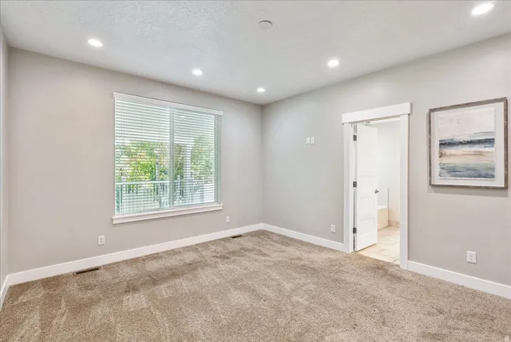 Recessed lighting, neutral wall paint, light-colored carpeting, a large window with blinds, and white trim