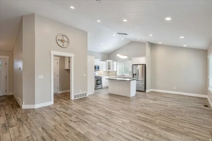 Vaulted ceilings with recessed lighting, tile-finish flooring, white cabinetry, stainless steel appliances, and a kitchen island with a dark countertop