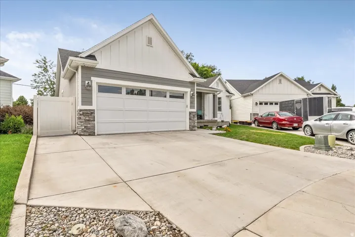 Exterior featuring gray siding, white vertical siding accents, stacked stone detailing, a two-car garage and a concrete driveway