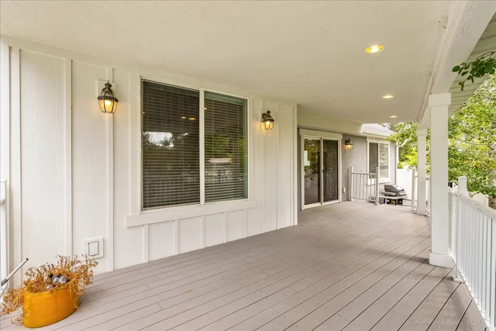 Covered outdoor deck with recessed lighting, board and batten siding, multiple windows with blinds, and white railing