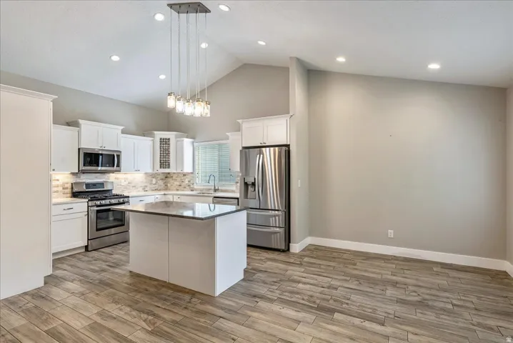 Vaulted ceiling kitchen with white cabinetry, stainless steel appliances, tile-finish backsplash, and tile-finish flooring