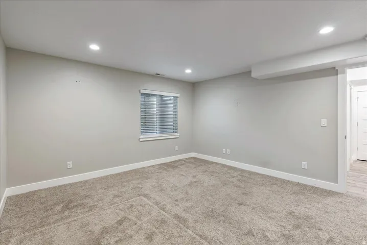 Spacious bedroom showcasing neutral wall finishes, recessed ceiling lighting, a large window with plantation shutters, neutral-toned carpet flooring