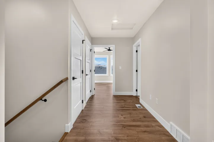 Hallway featuring wood-finish flooring, white panel doors with matte black hardware, and a wood handrail