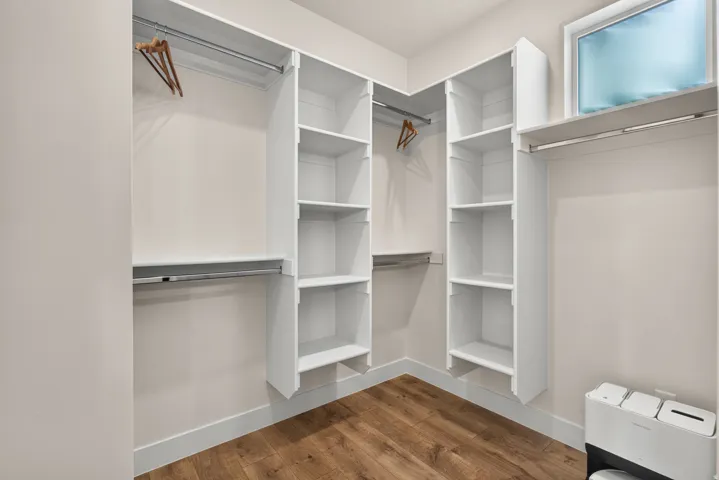 Built-in custom shelving, multiple hanging rods, corner configuration, wood-finish flooring, and a transom window