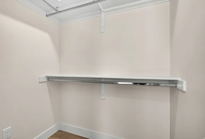 Closet featuring white shelving, a metal hanging rod, and wood-finish flooring