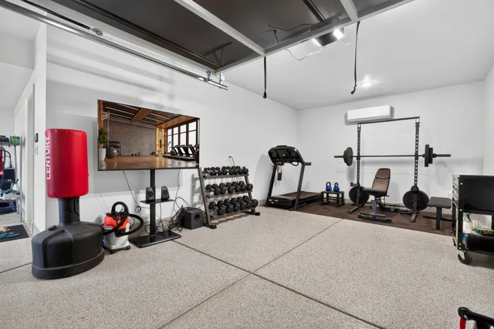 Epoxy flooring, white walls, exposed ceiling joists, wall-mounted air conditioning unit, and track lighting