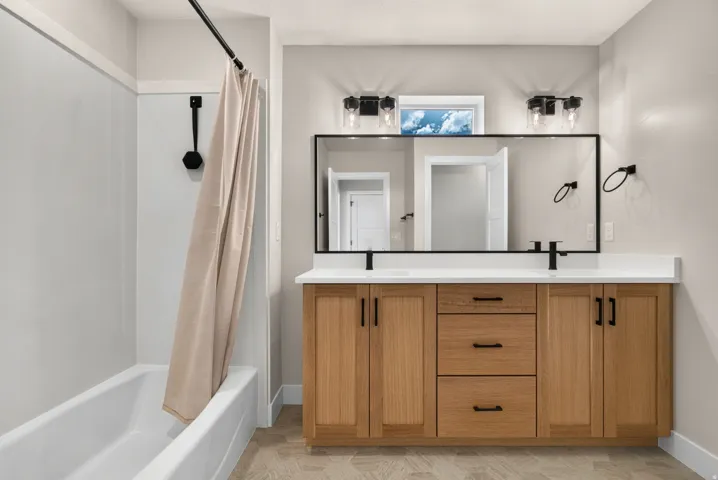 Double vanity with wood-finish cabinetry, white countertops, and matte black hardware