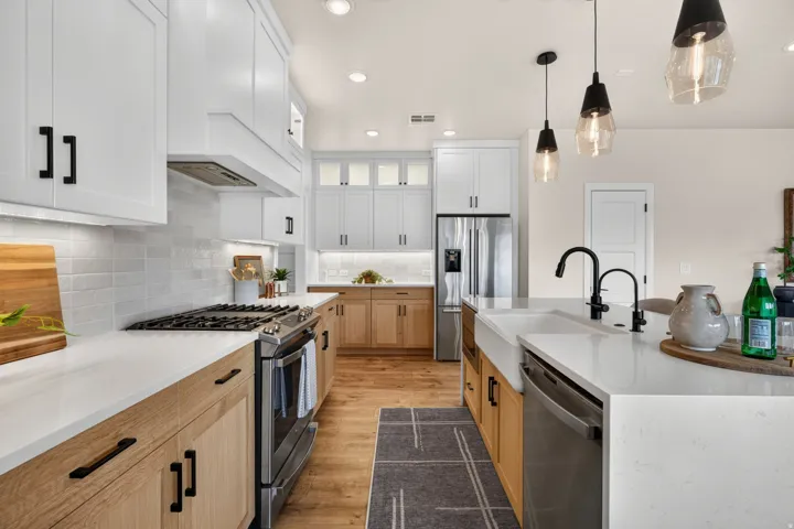 Modern kitchen featuring white shaker cabinetry, natural wood-finish lower cabinets, stainless steel appliances, a farmhouse sink, and pendant lighting