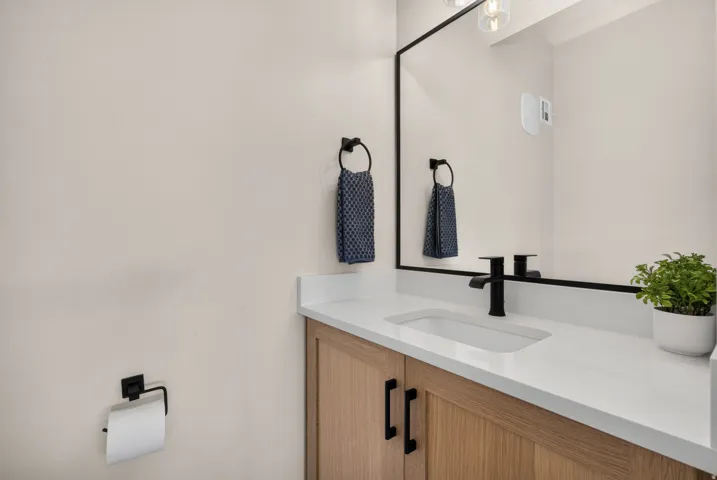 Wood-finish vanity with black hardware, white countertop, integrated rectangular sink, and matte black faucet