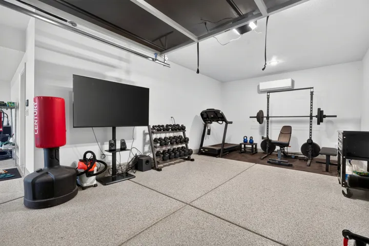 Epoxy-coated flooring, exposed ceiling joists, recessed lighting, and wall-mounted air conditioning unit