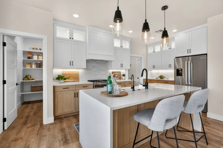 Modern kitchen featuring white shaker cabinetry, wood-finish flooring, a kitchen island with a light-toned countertop, and stainless steel appliances