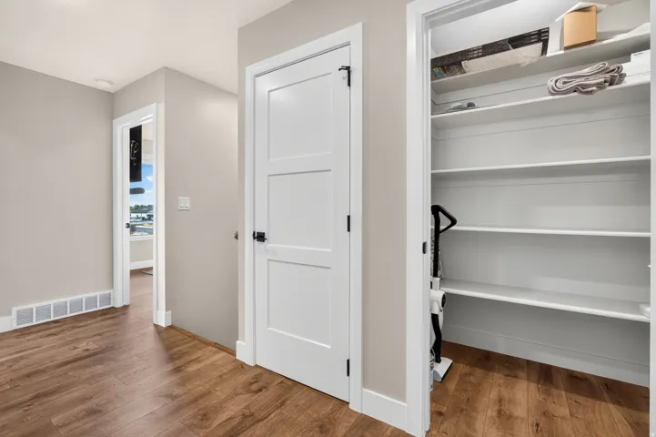 Wood-finish flooring throughout, bright white trim, three-panel interior doors with black hardware, and an open pantry with multiple shelves