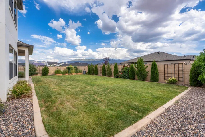 Expansive backyard featuring a manicured lawn, established landscaping, and a natural stone-finish gravel border