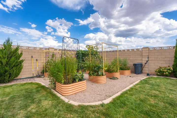 Landscaped backyard featuring raised garden beds, gravel path, manicured lawn, and perimeter block wall with decorative top
