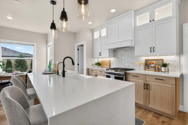 Modern kitchen featuring a large island with an integrated sink, white shaker-style upper cabinetry, wood-finish lower cabinetry, and a subway tile backsplash