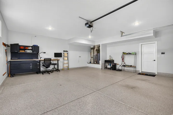 Spacious garage featuring a durable epoxy floor, integrated workbench, utility sink, and recessed lighting