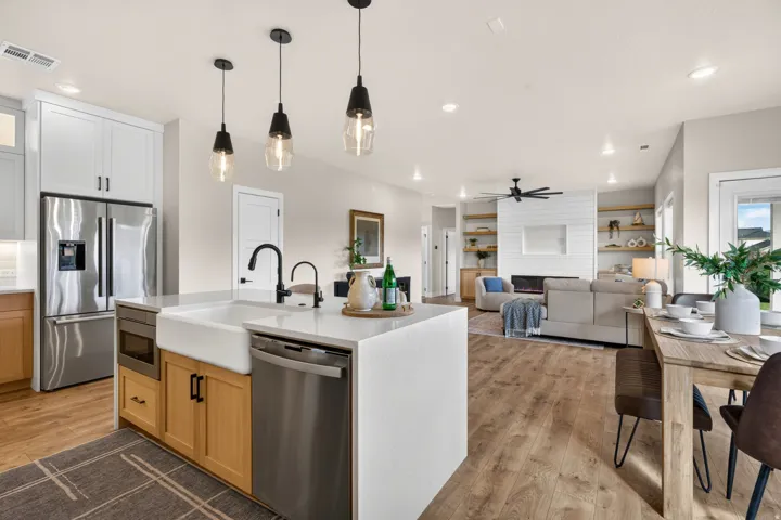 Open-concept kitchen and living area featuring wood-finish flooring, a kitchen island with a farmhouse sink, stainless steel appliances, and built-in shelving surrounding a fireplace