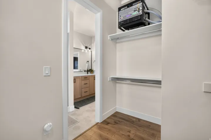 Walk-in closet with wood-finish flooring, two white shelves, and a chrome hanging rod
