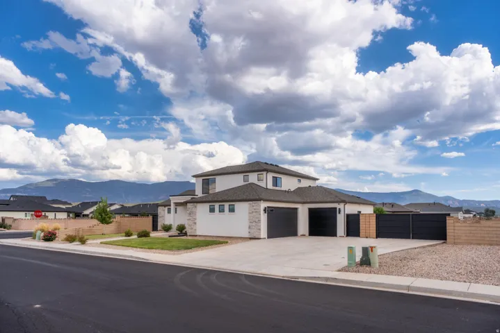 Contemporary stucco exterior, stone facade accents, dark shingle roof, dual garage doors, and a concrete driveway