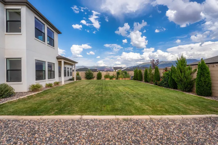 Expansive backyard featuring a manicured lawn, established landscaping, and a covered patio
