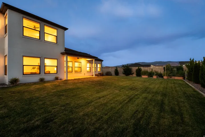 Expansive backyard featuring a manicured lawn, established landscaping, and a covered patio