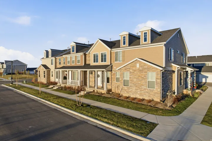 Exterior featuring stone veneer and siding, multiple dormer windows, covered porches with white columns, and a paved walkway