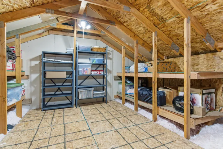 Attic space with exposed wood beam construction, oriented strand board ceiling, and natural light fixture