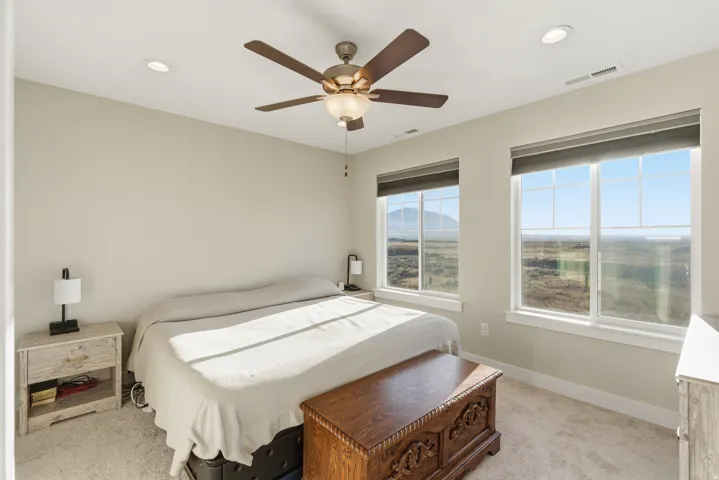 Recessed ceiling lighting, ceiling fan with integrated light, two large windows, roller shades, and wall-to-wall carpeting