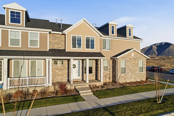 Multi-level townhouse with dormer windows, stone and siding exterior, front porch, and a manicured lawn