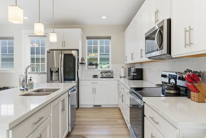 Kitchen featuring white shaker cabinetry, stainless steel appliances, light-toned countertops, wood-finish flooring, and pendant lighting