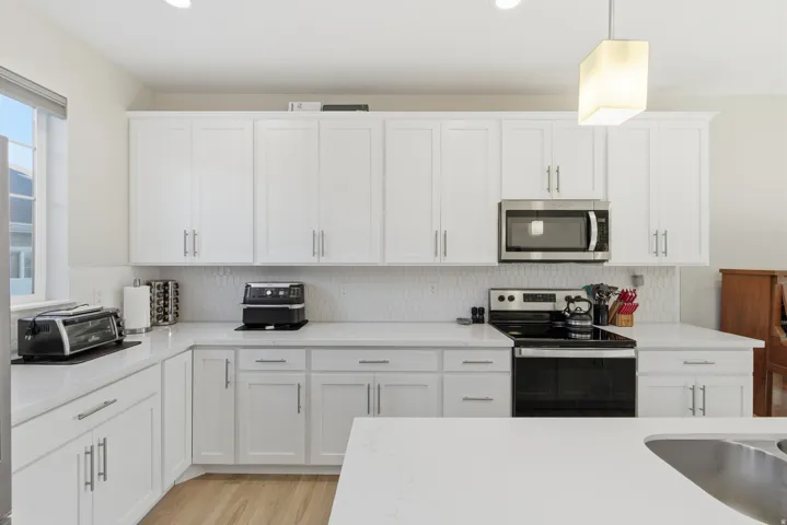 White shaker cabinetry, light countertops, integrated stainless steel appliances, hexagon tile backsplash, and recessed lighting