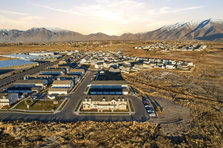 Community with a mountainous backdrop, featuring residential structures and paved roadways