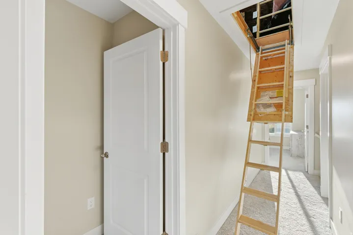 Attic access with a pull-down wooden ladder, white interior doors, and neutral wall paint